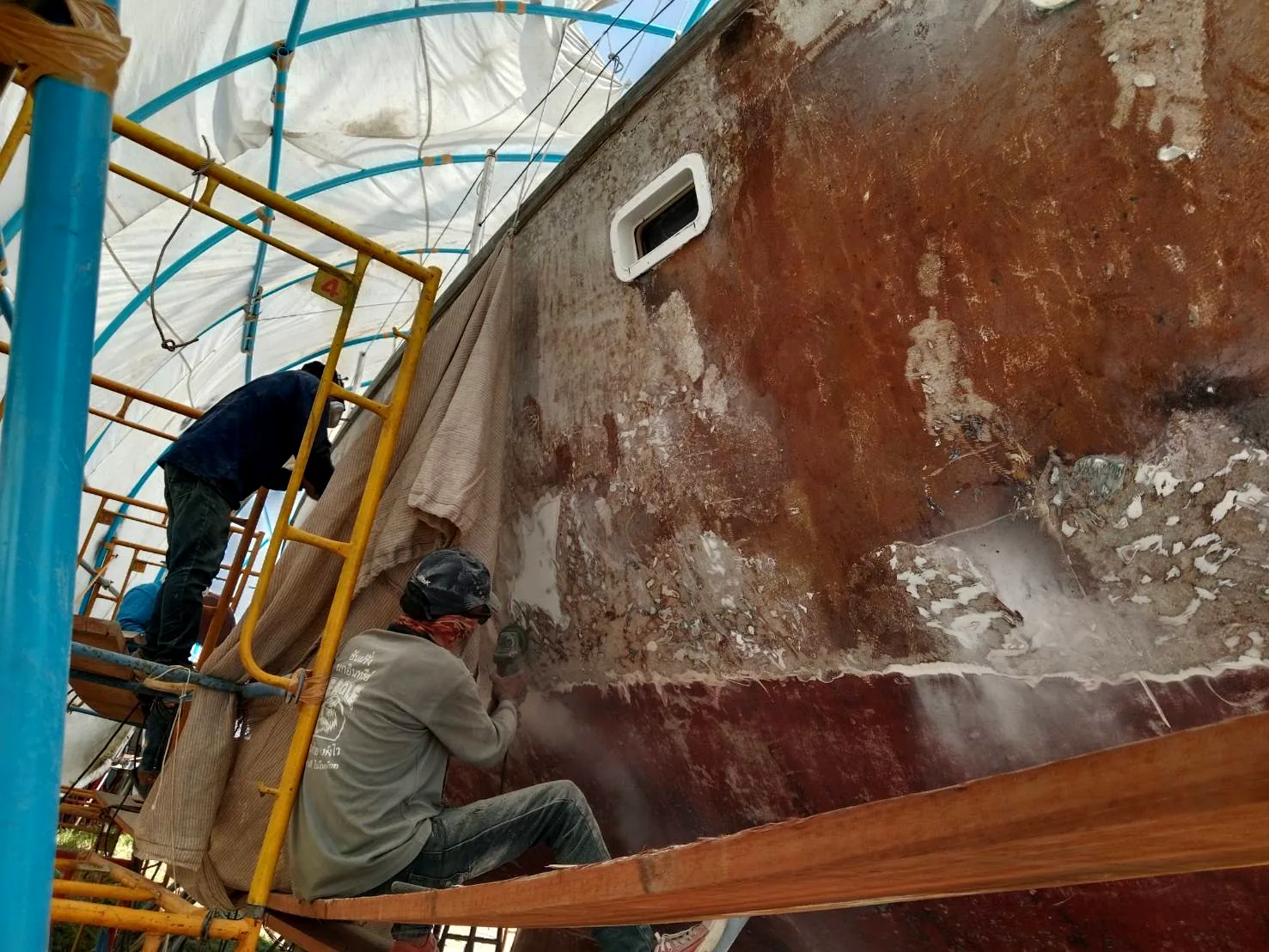 Workers sanding yacht hull on scaffolding