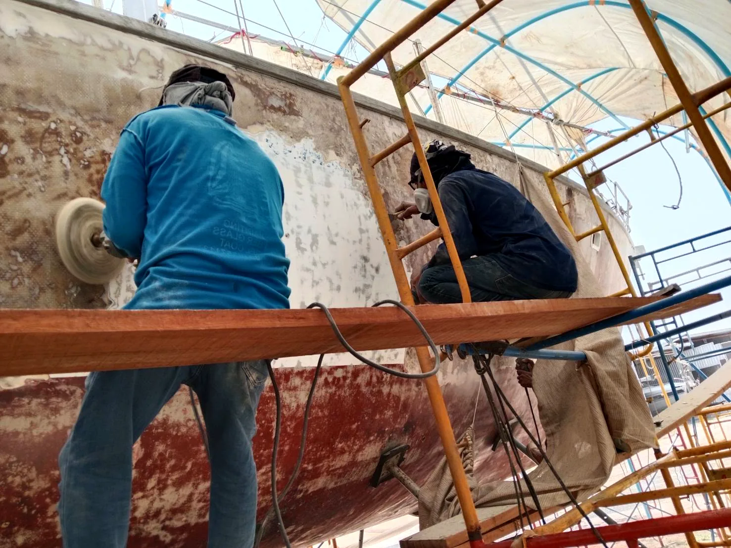 Two workers grinding hull with power tools